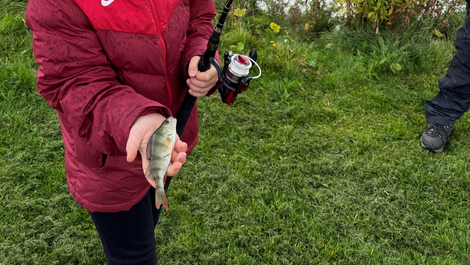 Barn med fiskestang og en fisk i hånden