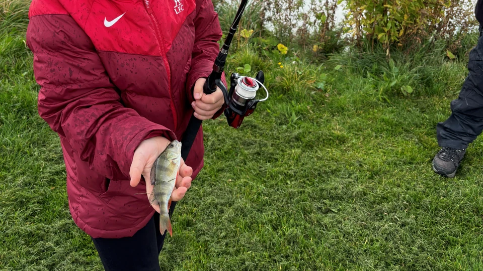 Barn med fiskestang og en fisk i hånden