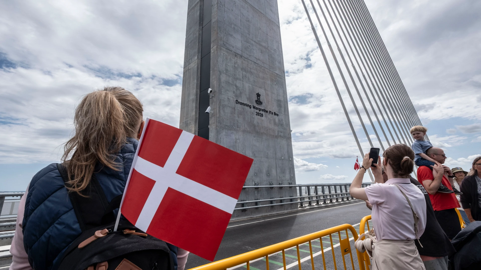 Billede af mennesker samlet med flag foran pylonen på en bro